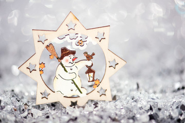 christmas bauble snowman in a star on silver background, wooden xmas decor for christmas tree. postcard concept with copy space and with place for text