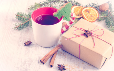 Obraz na płótnie Canvas Homemade christmas tree shaped cookie, pine, orange,cinnamon, anise and walnuts over white wood background. A cup of berry tea and a gift box wrapped in kraft paper. Christmas decoration.