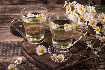 herbal chamomile tea on a wooden table. Chamomile tea in a transparent cup and camomile flowers on...