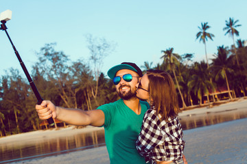 young beautiful couple making selfie photo on a selfie stick, hipsters, lovers together smile laugh photos on gopro, action camera, take pictures and shoot video at the beach,outdoor portrait,close up