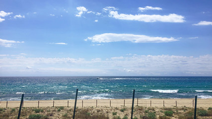 Obraz na płótnie Canvas Costa Brava Spain Catalonya beautiful seashore, a view from train on long mediterranean sea coastline with palms, people swimming and taking sun baths, strong waves with foam crashing over sand beach