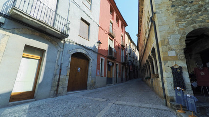 Fototapeta na wymiar BESALU CATALONIA SPAIN - JULY 2016: Smooth camera steady wide angle shot along narrow street in the old european spain village goes up, high colorful ancient walls with windows, clear sky with sun
