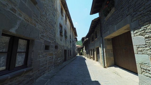 RUPIT CATALONIA SPAIN - JULY 2016: Smooth camera steady wide angle shot along narrow street in the old european spain village, high colorful ancient walls with windows, clear sky with sun