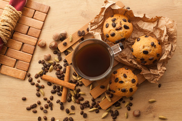 Fresh, just baked cupcakes with chocolate, cinnamon and coffee seeds set with cup of dark coffee on a wooden table. Good as late breakfast or lunch. Muffins with cup of americano and cardamom.