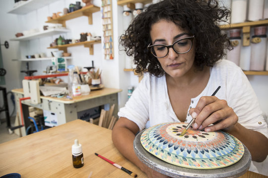 Woman painting a ceramic plate with a brush