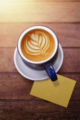 Cup of Coffee Latte on Wooden table with Blank Paper Note and Morning Sunshine light, selective focus on a cup