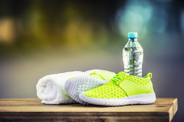 Pair of yellow green sport shoes towel water smart pone and headphones on wooden board. In the background forest or park trail.Accessories for running sport. - Powered by Adobe