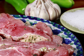 Detail of dish with turkey cutlets marinated with garlic and parsley in front of salt dish and a garlic bulb