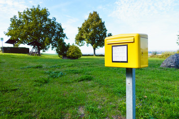 Yellow German postbox one in the green meadow in village