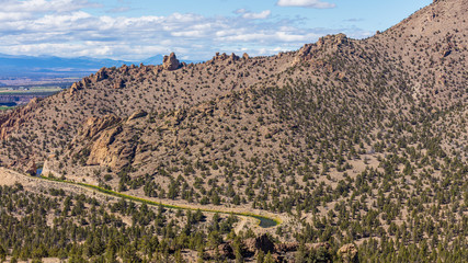 Brown rock slopes are covered with pine trees. The river flows between hills. Beautiful landscape of yellow sharp cliffs. Smith Rock state park, Oregon