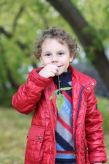 little curly cheerful boy walking in the woods among the trees and fallen yellow leaves in autumn