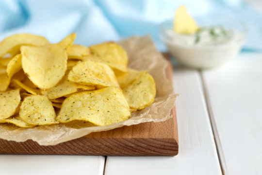 Potato chips with a dipping sauce on a white wooden table.