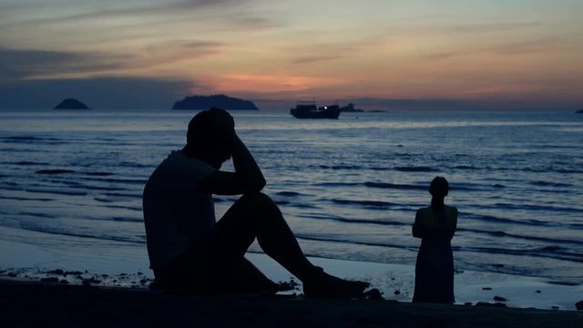 Silhouette of offended, conflicted couple on beach during sunset
