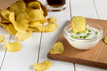 Potato chips in a paper bag and dipping sauce on a wooden table. - 122174498