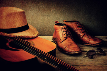 Still life with boots, hat, sunglasses and guitar on wooden table over grunge background. vintage...