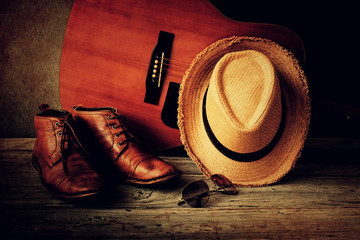 Boots with brown hat, sunglasses and guitar on wooden table over grunge background