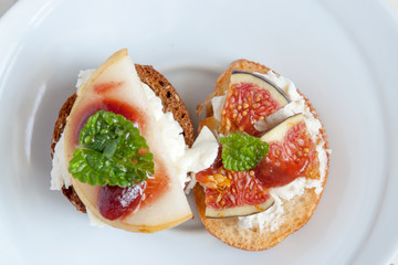 Bruschetta with goat cheese, pear and figs on white plate