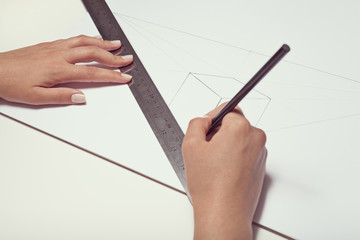 female hand drawing a cube with pen and ruler in two point perspective