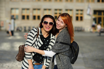 Two nice girls stand in the middle of the paved area having embraced.