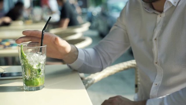 Man taking glass of mojito and drinking it in the outdoor cafe
