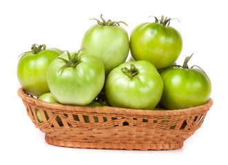 unripe green tomatoes in a wicker basket isolated on white background
