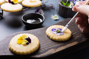 Process of making shortbread cookies with edible flowers on old wooden background. Holiday food