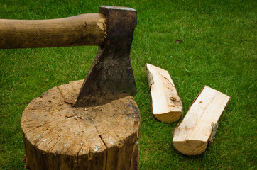 the axe has split a log/the axe has split firewood on a green grass
