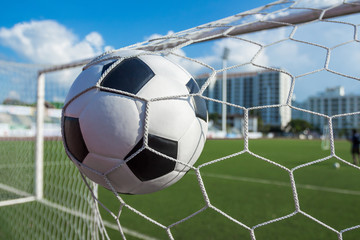 soccer ball in goal net with green grass blue sky