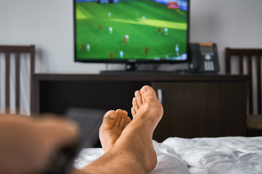 Man watching a television broadcast of a football match, lying in bed