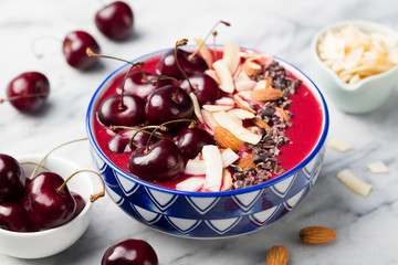 Smoothie bowl with fresh black cherries, coconut flakes, almond and cocoa nibs. Marble background