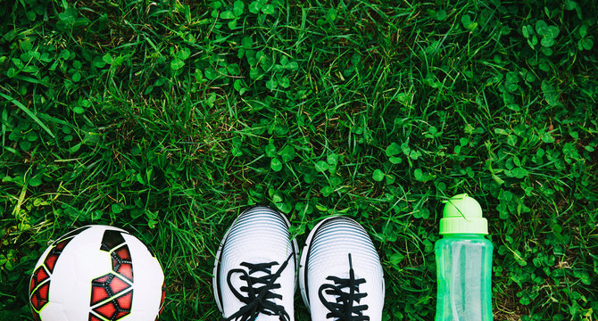Sports shoes sneakers, ball and bottle of water on a fresh green grass