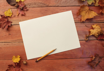 Autumn background with leaves of maple and Acorns a on wooden background. paper with a pencil in the autumn background, place for text.
