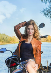 Fototapeta na wymiar Biker girl in a leather jacket and short shorts on motorcycle near the river