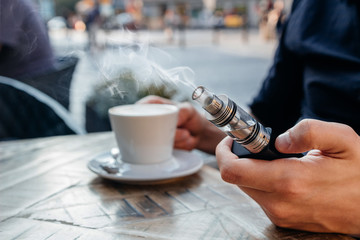 man using vape or electronic cigarette and drinking coffee