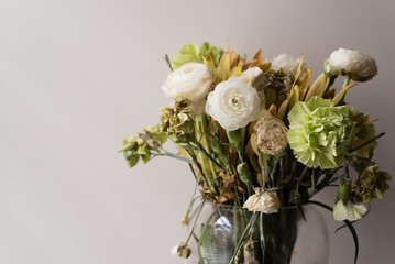 Close up of wilting green and white ranunculus and carnations in glass vase (selective focus)
