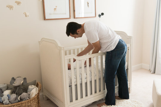 HIspanic Dad Putting Newborn Baby In Crib