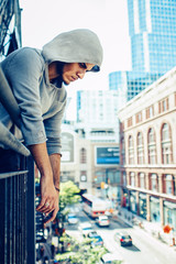 Conceptual art portrait of beautiful handsome pensive sad tired gothic young middle east brunette man with beard in hoodie, standing on staircase in city urban looking down on street