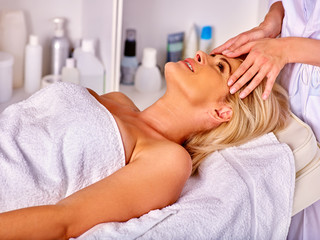Fototapeta na wymiar Woman middle-aged lying on bed and have face massage in spa salon.