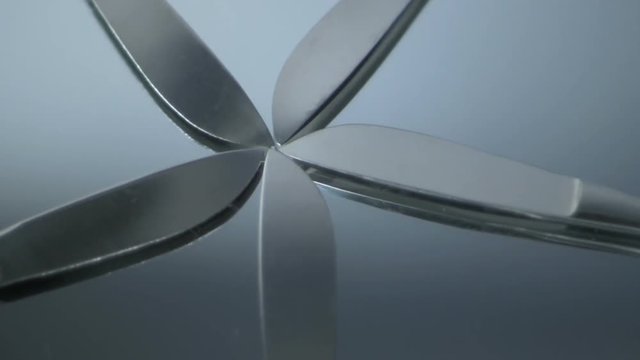 Five scalpels fanned out rotating counterclockwise on a glass mirror. HD 1080.