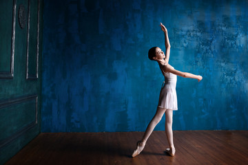 Young teenage ballerina is dancing and posing in the photostudio with blue walls