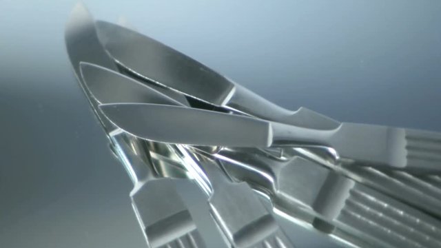Five scalpels rotating on a glass mirror. HD 1080.