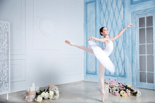 Young teenage ballerina is dancing and posing in the photostudio with blue and white walls