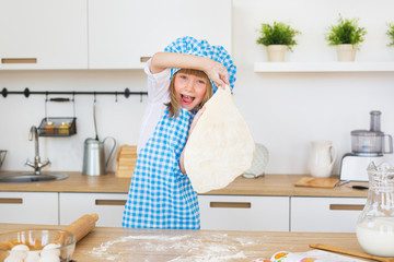 Pretty little girl in a cook clothes holds in a hands a circle of dough on a kitchen