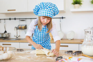 Little girl in a cook clothes kneads a dough on a kitchen