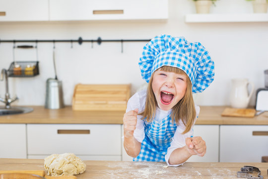 Portrait of pretty little girl in a cook looks funny screams a kitchen
