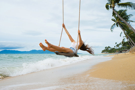 Vacation concept. Young woman  swing on a beach swing. Selective focus. Hairs in motion blur.