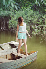 A young woman stands in an old wooden boat on the river, turquoise dresses, full length.
