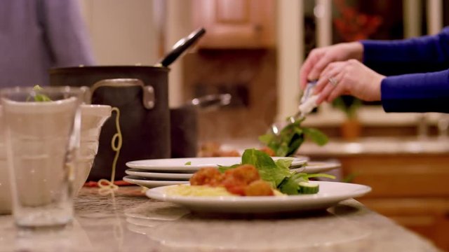 A mother and daughter dishing up salad, spaghetti and meatballs for dinner, close up