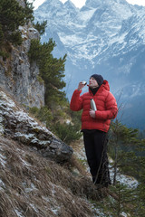 Mountaineer at winter snowy peaks background resting and drinking from vacuum flask metal cup