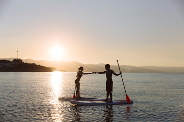 Silhouette of male and female on sup surf pull hands together at the ocean. Concept lifestyle, sport, love